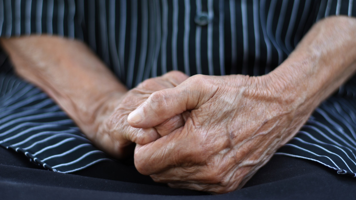 Close up of a midsection of an old woman, hand in hand in lap, wearing black short with white straps