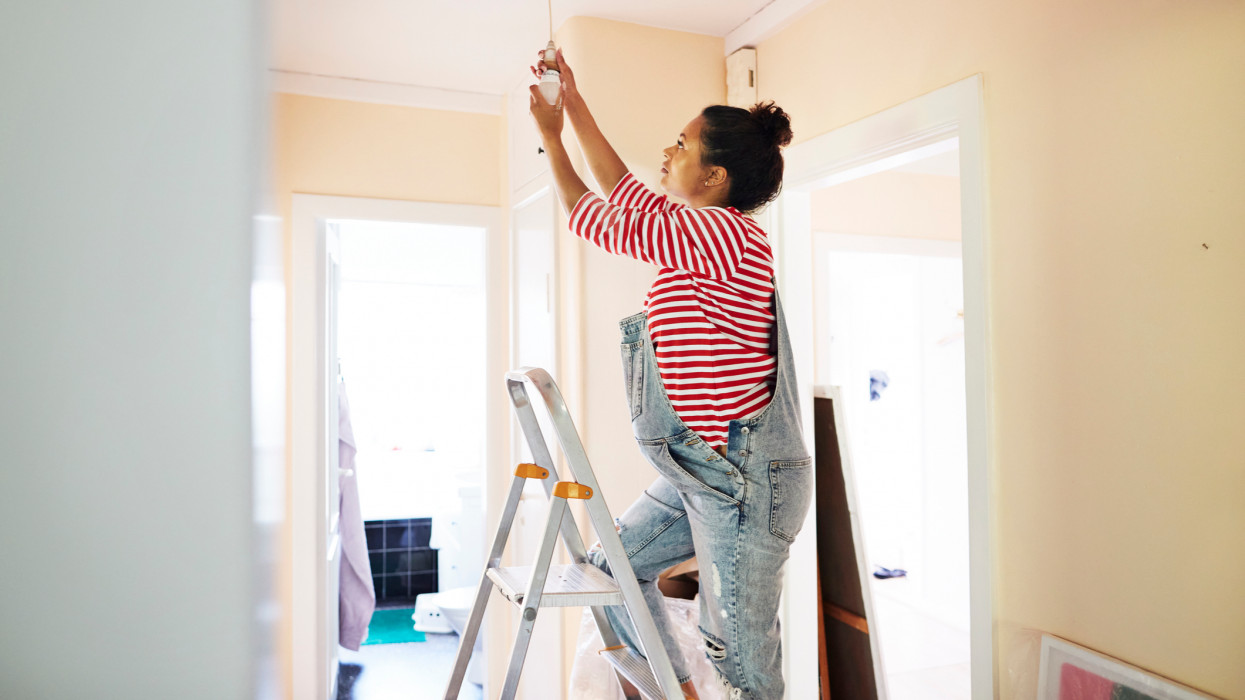 Pregnant woman changing light bulb on ceiling while standing on ladder
