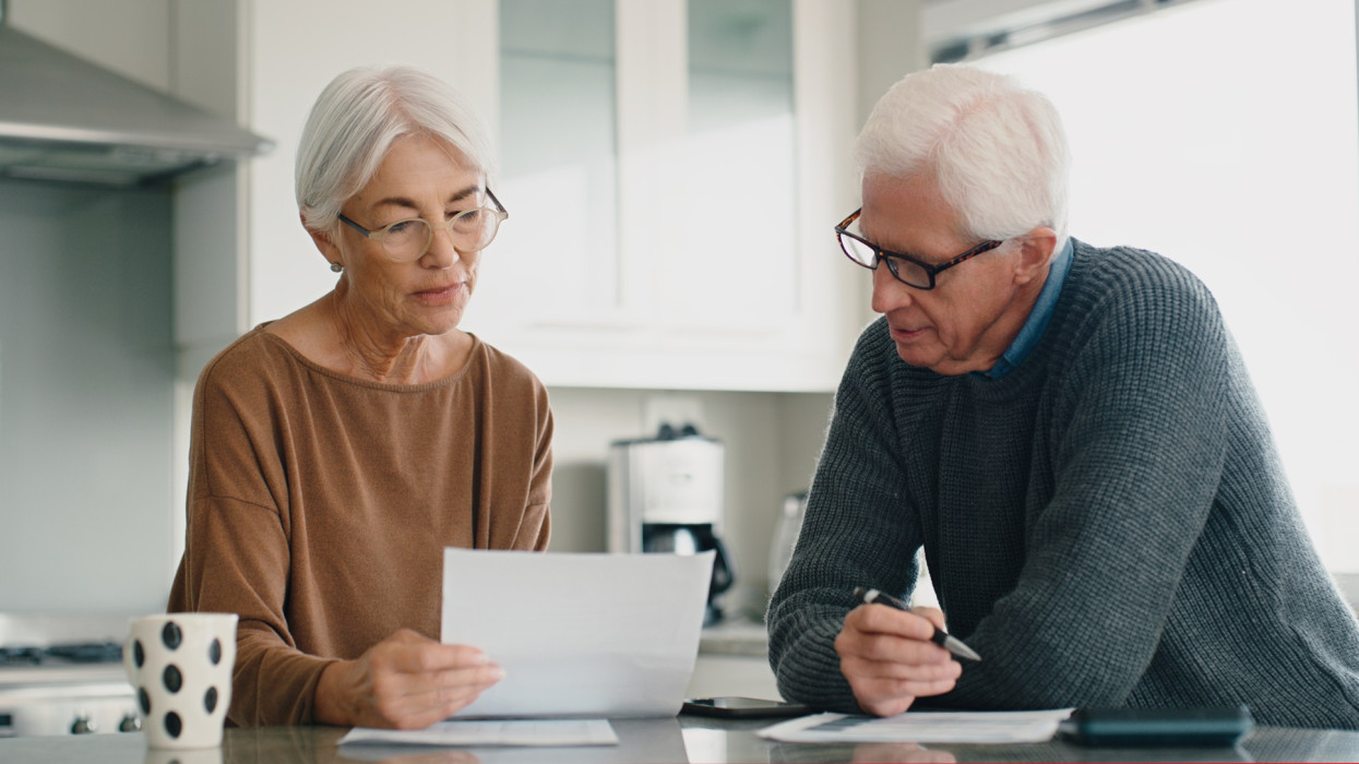 Senior couple, bills and budget in home for retirement savings, planning loan investment and financial administration. Old man, elderly woman and reading documents to review pension report in kitchen